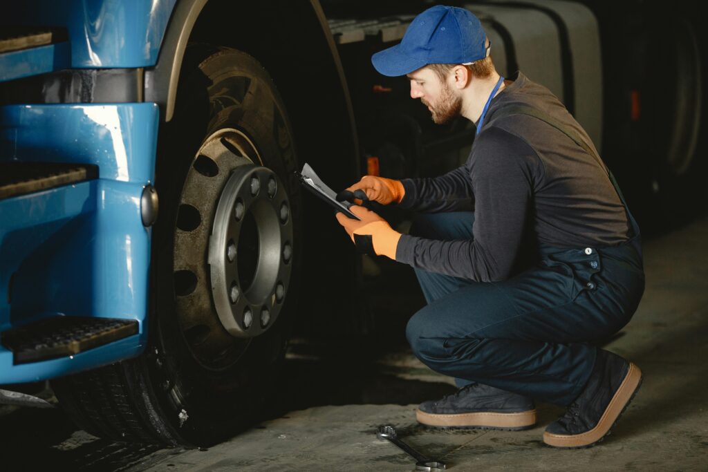 pexels-photo-6720537-6720537 Man in Blue Cap and Working Uniform Sitting Beside Truck Wheel and Reading a Paper